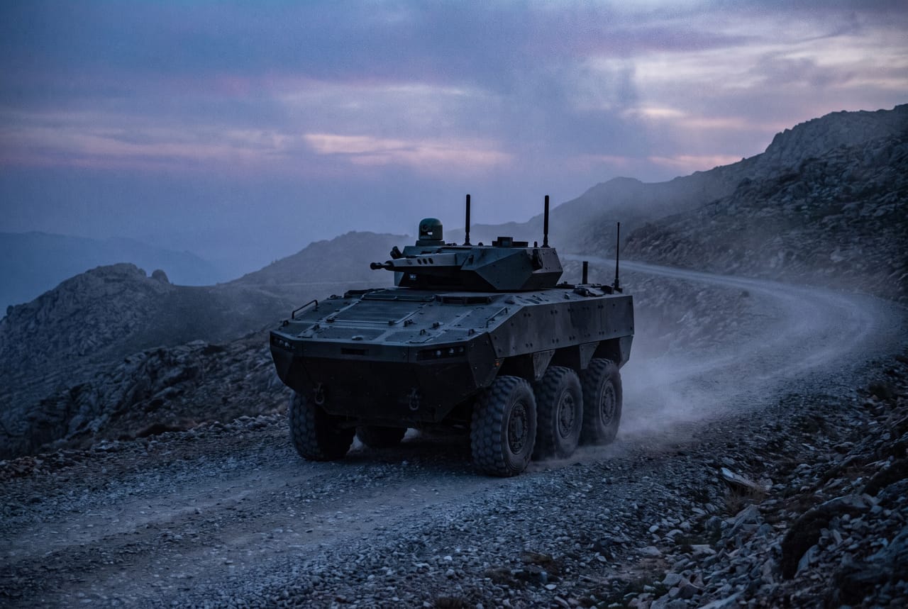 Unmanned armored vehicle with a sensor mast on a gravel mountain road